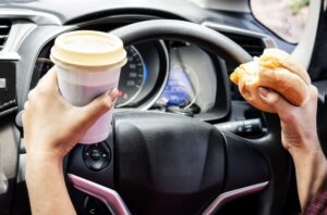 close-up of woman's hand, holding burger and coffee, engaged in reckless eating and drinking While driving car