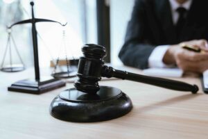 Judge’s gavel and scales of justice on a courtroom desk with a lawyer reviewing documents in the background.