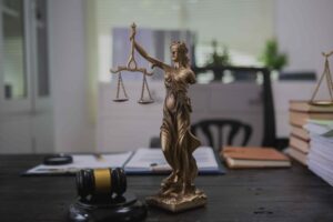 Bronze Lady Justice statue with scales of justice on a lawyer’s desk, alongside a gavel, legal documents, and case files.